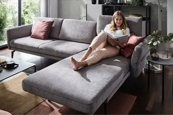 Graues Ecksofa, auf der eine Frau gemütlich liegt.