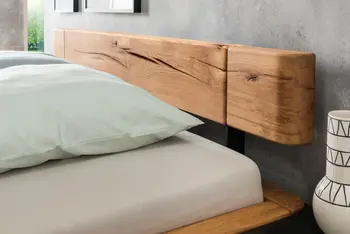 Kopteil eines Massivholzbettes, auf der Matratze liegt eine Decke mit grünem Bezug.