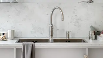 Moderne Edelstahl-Doppelspüle mit hohem Wasserhahn und grauem Handtuch an weißer Küchenzeile