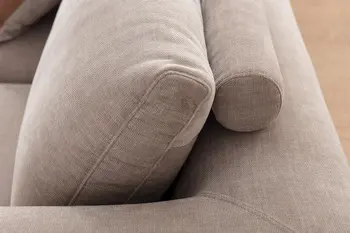 Seitliche Aufnahme eines grauen Sofas, das große dick gepolsterte Rückenkissen hat und dahinter runde Kopfstützen.