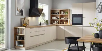 Cremefarbene Winkelkueche mit moderner Dunstabzugshaube und hoelzerner Arbeitsplatte.