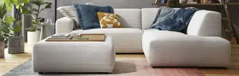 Modernes beiges Ecksofa mit Cordstoff bezogen und einem passenden Hocker, auf dem Sofa sind mehrere Kissen in blau und gelb.