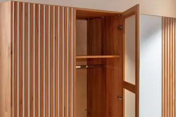 Kleiderschrank aus hellem Holz mit Lamellenakzenten und weißen Elementen zwischen den Lamellen mit einer geöffneten Türe, die den Blick auf eine Kleiderstange freigibt.