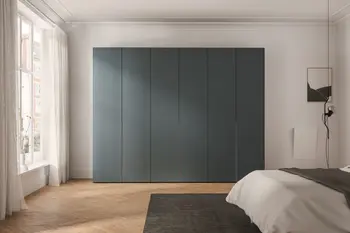 Moderner salbeigrüner Drehtürenschrank mit sechs Schranktüren in einem hellen Raum mit großem Fenster.