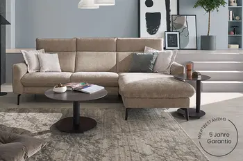 Beiges Ecksofa in Wohnzimmer mit rundem Couchtisch, beigem Teppich und hellblauer Wand.