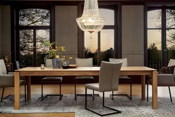 Großer Massivholz Esstisch in einem Raum mit großen Fenstern, um den Tisch stehen mehrere graue Freischwinger und Armlehnstühle.