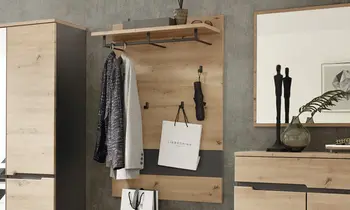 Garderobenpaneel aus hellem Holz mit Stange zum Aufhängen von Kleidung und einem Regal obendrüber, um Sachen zu verstauen. Stange, Harken sowie ein Teil der Rückenplatte sind in Schwarz gehalten, um Akzente zu setzen.&nbsp;