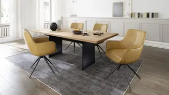 Moderne gelbe Armlehnstühle mit schwarzem Metallgestell um einen Massivholz Esstisch in einem hellen Esszimmer.