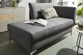 Graues Sofa mit Schlaffunktion, auf dem ein buntes Kissen und aufgeschlagenes Buch liegen in einem hellen Raum.