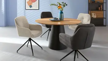 Helles Wohnzimmer mit rundem Tisch und vier verschiedenfarbigen Sesseln. 