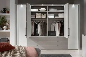 Großer Weißer Kleiderschrank mit Türen links und rechts, in der Mitte sind im unteren Teil sechs Schubläden, darüber zwei Türen die geöffnet sind und Kleidung zeigen.