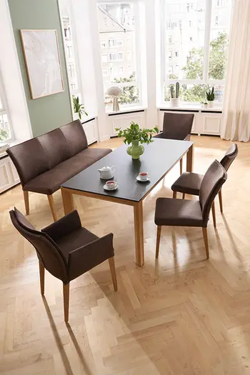 Klassisch eingerichtetes Esszimmer mit großem Esstisch und Sitzbank mit Stühlen in braunem Stoffbezug.