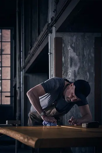 Ein Mann wischt bei der Produktion eines Esstisches über die Massivholz Tischplatte.