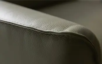 Nahaufnahme einer Sofalehne aus hochwertigem Echtleder in Olivgrün – fein genarbte Oberfläche mit eleganter Steppnaht für exklusiven Sitzkomfort und stilvolles Design.