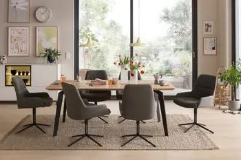 Esstisch aus Massivholz mit schwarzem Gestell um den graue Stühle mit schwarzen Beinen stehen in einem hellen Raum.