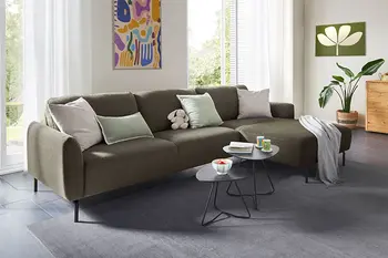 Grünes Ecksofa mit filigranen schwarzen Beinen. 