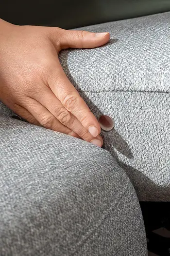 Detailbild von motorischer Relaxfunktion per Knopfdruck bei hellgrauem Sofa.