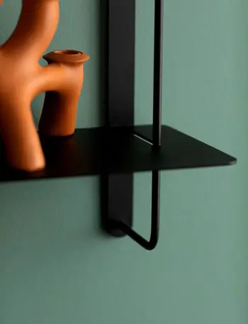 Moderne Deko in der Farbe Terrakotta auf einem schwarzen Wandregal an grüner Wand.