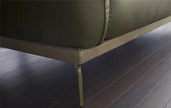 Detailaufnahme eines modernen Sofafußes aus Metall – schlanke, elegante Linienführung in Kombination mit dunkelgrünem Lederbezug und hochwertigem Holzboden für ein stilvolles Interieur.