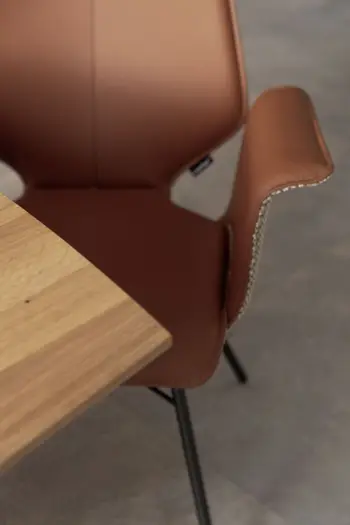 Moderner Design Esszimmerstuhl mit Armlehne, der auf der Innenseite einen Lederbezug in rose hat und leicht weggedreht von einem Holztisch steht.