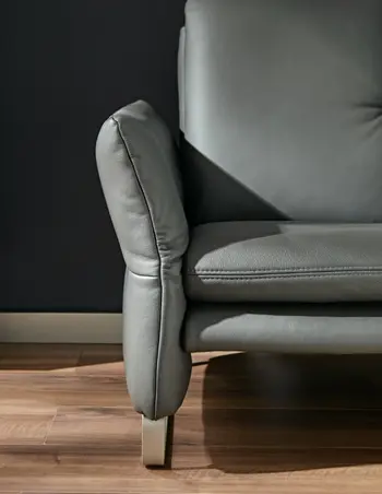 Graue leicht schräge Armlehne eines Ledersofas mit silbernen Kufen.