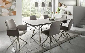 Modernes Esszimmer mit stilvollem Esstisch in Betonoptik und sechs gepolsterten Drehstühlen – minimalistisches Design, lichtdurchfluteter Raum und gemütliche Atmosphäre für stilvolle Mahlzeiten.