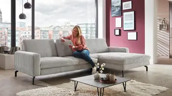 Frau liest Zeitung auf hellgrauem Stoffsofa in Wohnzimmer mit großem Panorama-Fenster.