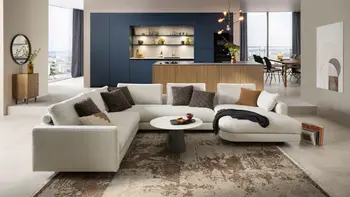 Hellbeiges Design Ecksofa vor einer Designküche mit Kücheninsel in Holzlook und blauen Hochschränken.