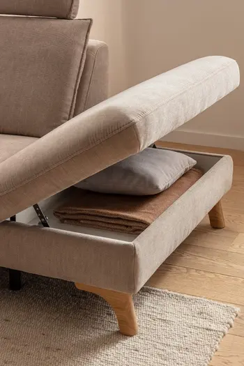 Beiges Sofa, bei dem die Sitzfläche auf der rechten Seite nach oben geklappt ist und Stauraum sichtbar ist.