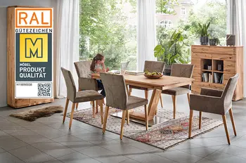 Qualitätssiegel "Goldene M" auf einem Bild von einem Esszimmertisch, Vitrine und Highboard aus Massivholz in einem gemütlichen Esszimmer, ein Mädchen sitzt am Esstisch vorm Laptop.