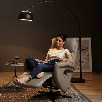 Frau entspannt in einem modernen Relaxsessel aus Leder mit verstellbarer Rückenlehne – gemütliche Leseecke mit Bogenlampe, Teppich und Beistelltisch für stilvolles Wohnzimmerambiente
