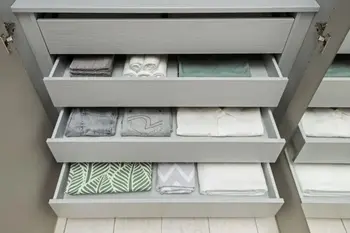 Drei geöffnete mit Kleidung befüllte graue Schubladen eines Kleiderschranks.