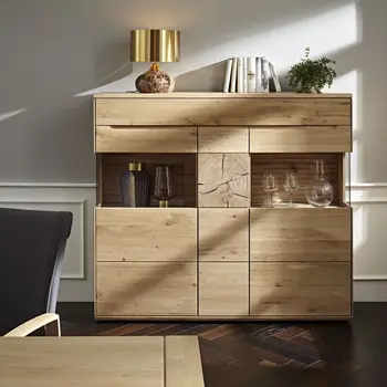 Modernes Highboard aus Massivholz mit sichtbarer Holzmaserung an der Front und zwei beleuchtete Glaseinsätze, in denen Gläser und Vasen stehen.