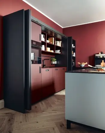 Eine Pocket-Küche von next125 mit roten Fronten und schwarzen Korpussen. Vor der Küche steht eine Insel mit weißer Verkleidung.&nbsp;