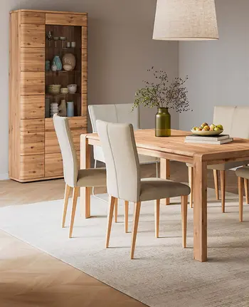 Natürlich eingerichtetes Esszimmer mit Holztisch, Vitrine aus Massivholz und beigen Esszimmerstühlen.