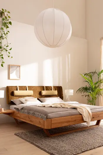 Bett mit Holzrahmen und Kopfteil aus grünem Polster in einem hellen Schlafzimmer mit Pflanzen und gemütlicher Einrichtung.