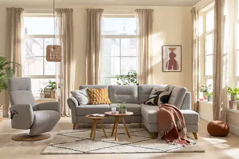 Graues Ecksofa mit bequem gepolsterten Rückenpolster und zwei Kopfstützen neben einem grauen Relaxsessel in einem gemütlichen Wohnzimmer.