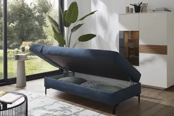 Blaues Sofa, das zur Liegefläche umgeklappt ist und Stauraum unterhalb der Sitzfläche hat.