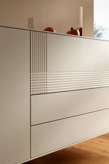 Weißes Designer Sideboard mit einer Türe und drei Schubladen, an der Front der obersten Schublade sind Rillen.