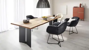 Dick gepolsterte Stuhlsessel in schwarzem Leder und einer mit weißem Fell um einen modernen großen Massivholz Esstisch.