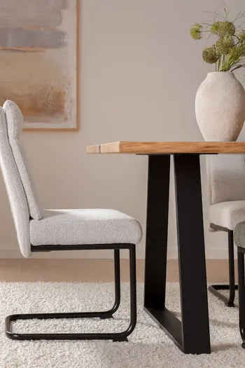 Weißer Freischwinger mit schwarzem Metallgestell, der an einem Massivholztisch steht.