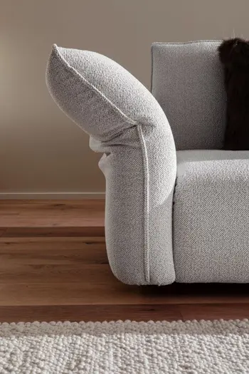 Abgeknickte Armlehne eines grauen Sofas.