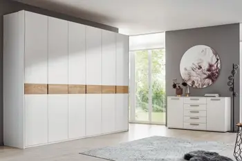 Großer weißer Kleiderschrank mit sechs Türen und Akzenten in Holz Optik und eine weiße Kommode mit grauen breiten Griffen.