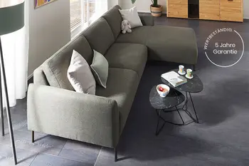 Gemütliches Wohnzimmer mit grünem Ecksofa und grauen Beistelltischen.