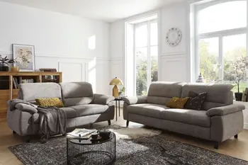 Zwei graue Sofas mit klappbaren Kopfstützen, die im rechten Winkel nebeneinander stehen in einem hellen gemütlichen Raum.