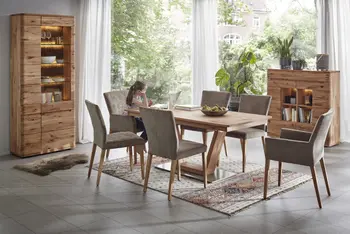 Esstisch aus Holz mit einem metallischen Fußteil, an dem ein Kind vor einem Laptop sitzt auf einem braunen Armlehnstuhl und daneben weitere Polster-Stühle mit und ohne Armlehne in braun.