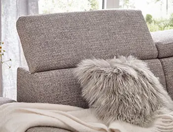 Graues Sofa mit aufgestellter Kopfstütze und einem flauschigen grauen Kissen und einer weißen Decke.