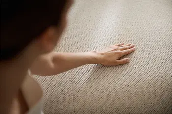 Frau streicht mit Hand über legere, weiche Polsterung bei beigem Ecksofa.