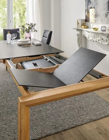 Esstisch mit schwarzer Tischplatte, bei dem eine Verlängerung angebracht wird.