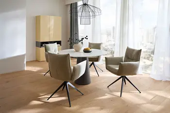 Offener Essbereich mit rundem Tisch in Marmoroptik und vier Armlehnstühlen in grünem Stoff.